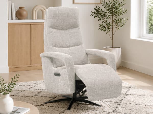 Light gray fabric recliner chair with extended footrest in a bright living room near a window and plants, on a shag rug.