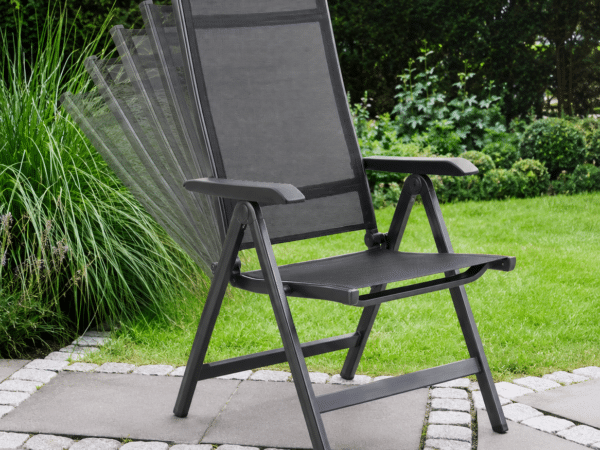 Black outdoor mesh armchair on a stone-patio, with a green lawn and hedges in the background.