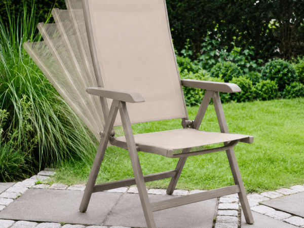 Beige folding garden chair on a stone patio with a green lawn and hedges in the background, shallowly in focus.