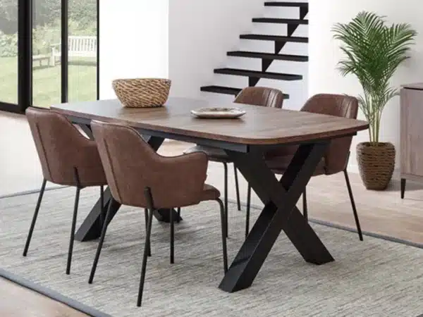 Rectangular wooden dining table with black crisscross legs, surrounded by six brown upholstered chairs in a bright modern dining room; a woven basket sits on the table and a tall plant is nearby.